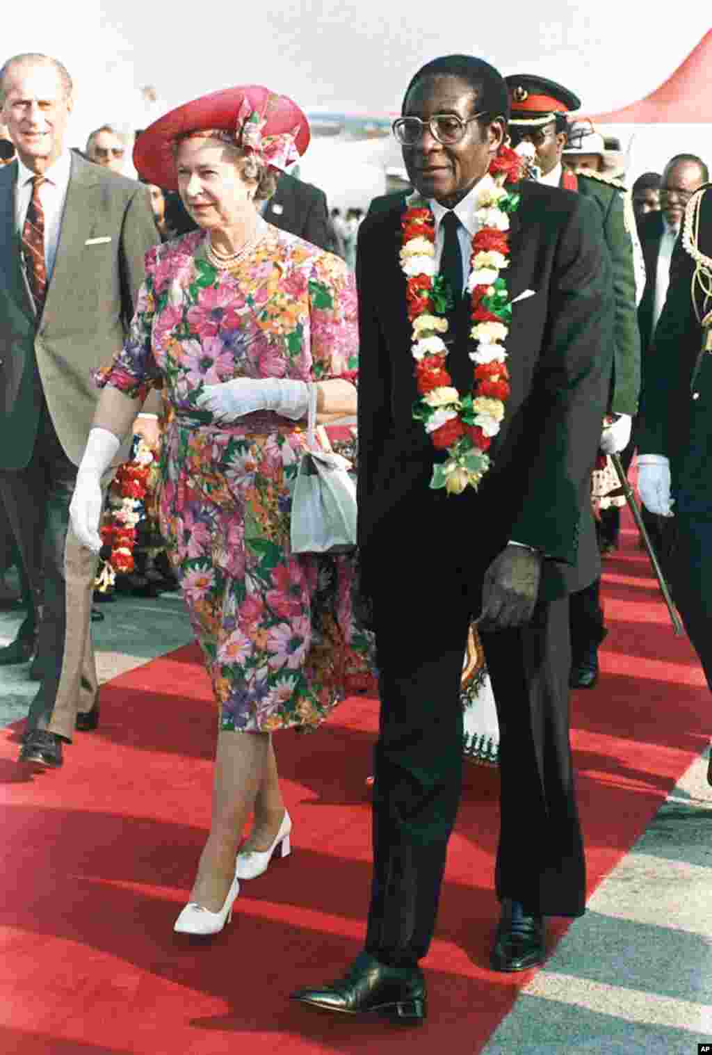 In this file photo taken Oct. 10, 1991 Britain's Queen Elizabeth II is escorted by Zimbabwean President Robert Mugabe, right, after the Queen's arrival at Harare airport on a second visit to the country. 