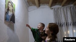 Hevin Gilo di hembêza xwe de qîza xwe ya bi navê Jîna, li wêneya daliqandî ya Jîna Emînî dinlêre. (Qamişlo, 13/09/2023)