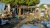 People stand near the wreckage of a car and kiosks after a bombing in Mogadishu, Somalia, Sept. 29, 2023.