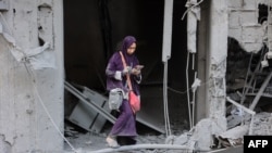 FILE - A woman checks her phone as she stands amid the rubble of a building destroyed during Israeli bombardment in Gaza City's Sheikh Radwan neighborhood, Aug. 11, 2024.