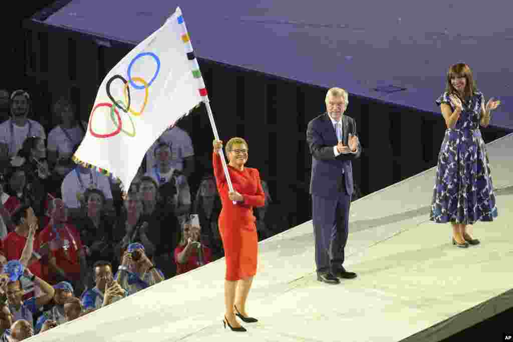 Los Angeles Mayor Karen Bass, left, holds a Olympic flag as IOC President Thomas Bach, center, and Paris Mayor Anne Hidalgo, right, look on during the 2024 Paris Olympics closing ceremony at the Stade de France, Aug. 11, 2024, in Saint-Denis, France.