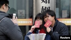 一對年輕人在北京一處婚姻登記處外手舉結婚證留影。（2017年2月14日）