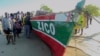 In this video grab, people stand next to a boat that local media say capsized the day before off Mozambique's Nampula province, April 8, 2024. (Television Mozambique via AP)