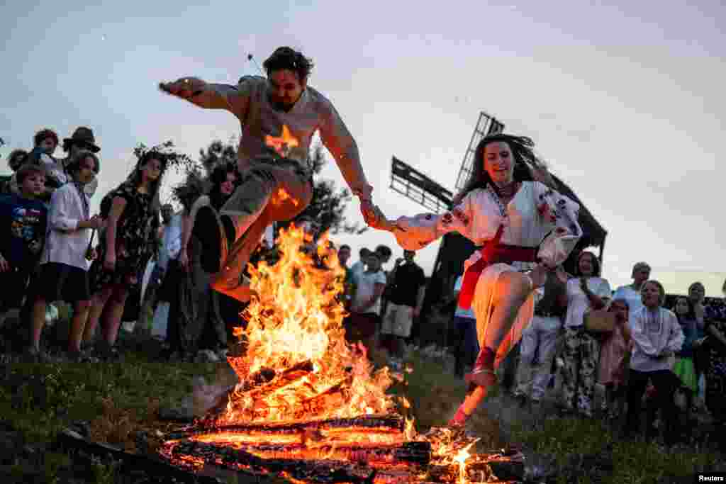 People jump over a campfire during a celebration on the traditional Ivana Kupala (Ivan the Bather) holiday in the village of Vytachiv in Kyiv region, Ukraine, amid Russia's attack on Ukraine, June 22, 2024. The ancient tradition, originating from pagan times, is marked with grand overnight festivities during which people sing and dance around campfires, believing it will purge them of their sins and make them healthier