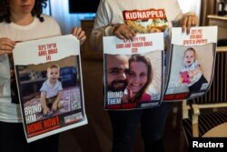 Ofri Bibas Levy, yang saudara laki-lakinya Yarden (34) disandera bersama istrinya Shiri (32) dan 2 anaknya Kfir (10 bulan) dan Ariel (4), memegang foto mereka bersama temannya Tal Ulus di Jenewa, Swiss, 13 November 2023. (Foto: REUTERS/Denis Balibouse)