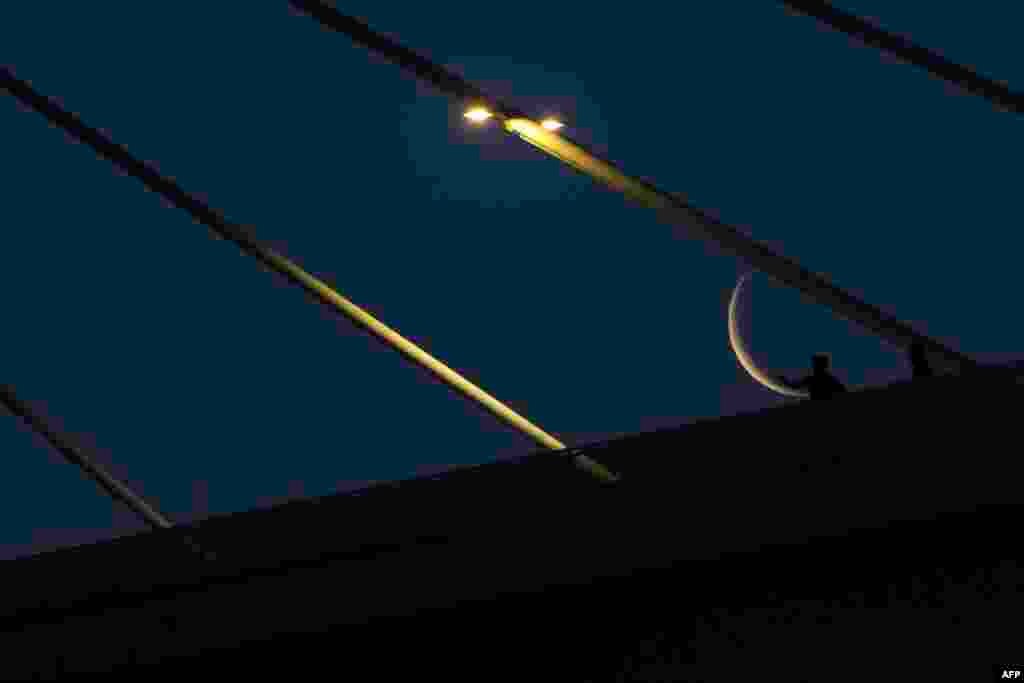 The waning crescent moon, near the end of the Muslim holy month of Ramadan, is pictured behind the Mohammad Baqir al-Sadr bridge in Iraq's southern city of Basra.