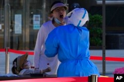 A woman opens her mouth for a swab sample during mass COVID-19 testing, in Beijing, May 3, 2022.