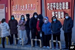 北京市民在宣传习近平思想的标语墙前排队等候接受核酸检测。（2022年12月5日）