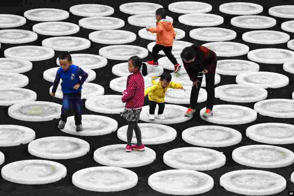A woman watches as children play on the light circles on display at the capital city's popular shopping mall in Beijing, China.