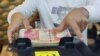 FILE - A man counts Iraqi dinars on a money counting machine at a currency exchange shop in Baghdad, Iraq, Jan. 23, 2023. 