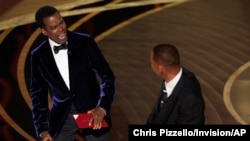 Presenter Chris Rock, left, reacts after being hit on stage by Will Smith while presenting the award for best documentary feature at the Oscars on Sunday, March 27, 2022