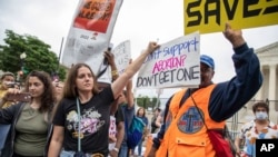 2022年5月14號，支持和反對婦女墮胎權利的美國民眾聚集在美國最高法院外舉行抗議活動。一名支持墮胎權利的女士試圖用手裡的標語牌遮蓋她身旁一位反對墮胎的抗議人士手中的標語板。 -照片來自美聯社