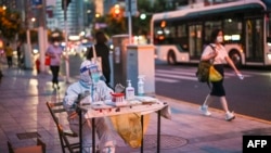 A health worker waits to test people for the COVID-19 coronavirus on a street next to a residential area in the Jing'an district of Shanghai on July 5, 2022.