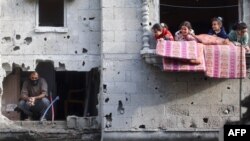 Deca se igraju na balkonu stana pored čoveka koji proverava razmere razaranja posle izraelskog udara u kampu Nuseirat, u centralnom pojasu Gaze, 10. decembar, 2024. (Foto: AFP/Eyad Baba)