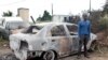 In this April 19, 2015, photo a foreign national from Zimbabwe stands by one of his two cars set alight after he survived a petrol bomb attack at his home in Illovo, some 55 kilometers south of Durban, South Africa. Tensions are high in South Africa’s capital, Feb. 20, 2017, amid a wave of attacks against businesses owned by immigrants.