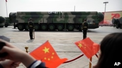 FILE - Para penonton mengibarkan bendera China ketika kendaraan militer yang membawa rudal balistik DF-41 meluncur dalam parade di Beijing, China, 1 Oktober 2019. China telah memperluas kekuatan nuklirnya jauh lebih cepat dari perkiraan para pejabat AS.