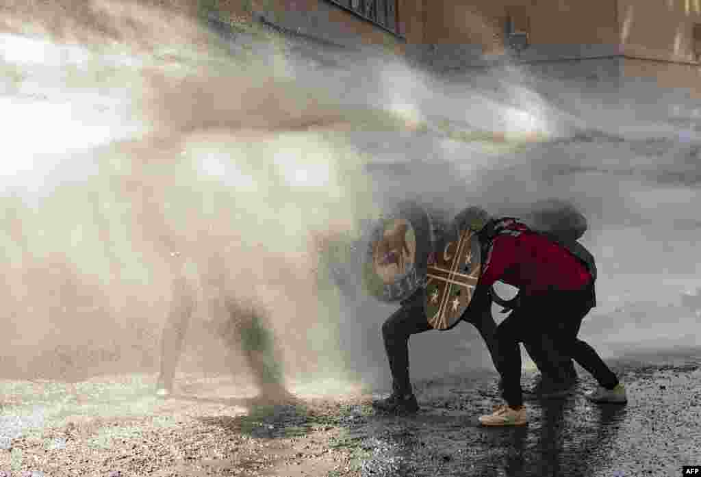 Demonstrators use shields to protect themselves from water sprayed by riot police during clashes on the marking of the first anniversary of the social uprising in Chile, in Santiago, Oct, 18, 2020.
