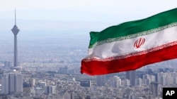 FILE - In this March 31, 2020, file photo, Iran's national flag waves as Milad telecommunications tower and buildings are seen in Tehran, Iran. 