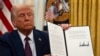 President Donald Trump holds up a signed executive order relating to the Lumbee Tribe of North Carolina in the Oval Office of the White House, Thursday, Jan. 23, 2025, in Washington. (AP Photo/Ben Curtis)