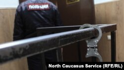 A Russian policeman stands by as a pair of handcuffs hang from a rail. 