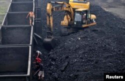 A labourer (L) walks on the edge of cargo train carriages as his colleagues shovel coal at a coal dump site