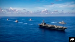 In this photo released by the U.S. Navy, the Nimitz-class aircraft carrier USS Carl Vinson (CVN 70), the Ticonderoga-class guided-missile cruiser USS Lake Champlain (CG 57), and the Arleigh Burke-class guided-missile destroyer USS Chafee (DDG 90) conduct a passing honors ceremony with the Japan Maritime Self-Defense Force (JMSDF) Murasame-class destroyer JS Ikazuchi (DD 107) and the Kongo-class guided-missile destroyer JS Chokai (DDG 176) in the Pacific Ocean, Sept. 19, 2021.