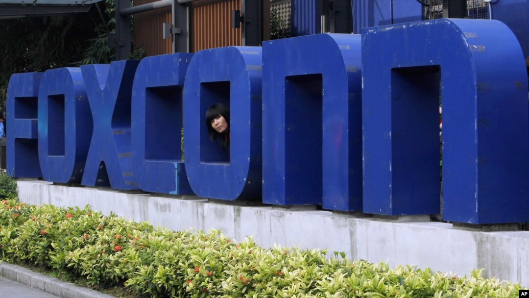 FILE - A worker looks out through the logo at the entrance of the Foxconn complex in the southern Chinese city of Shenzhen, May 27, 2010. 