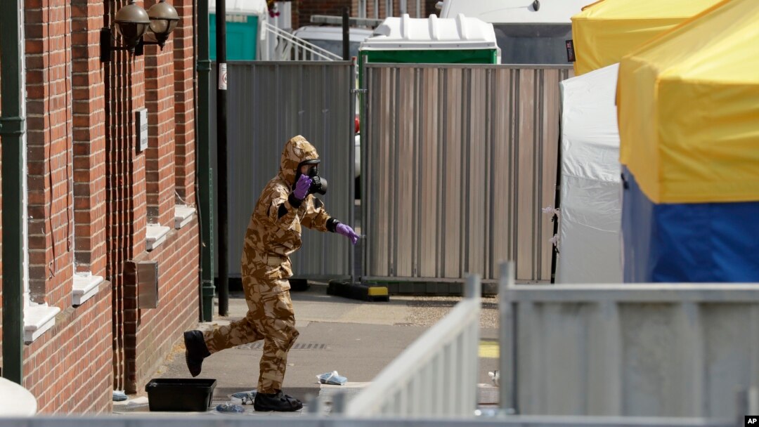A specialist team member in a military protective walks away after standing in a foot bath as they leave the front entrance of John Baker House for homeless people on Rollestone Street in Salisbury, England, Friday, July 6, 2018. 