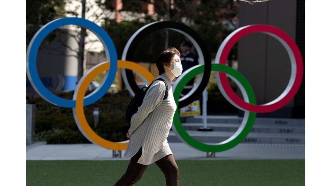 FILE - A woman wearing a protective face mask amid an outbreak of the coronavirus walks past Olympic rings displayed in front of the Japan Olympics Museum, in Tokyo, Japan, March 13, 2020.