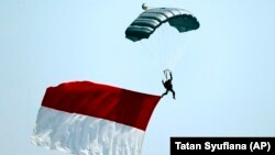 Seorang tentara melompat dengan parasut sambil membawa bendera Merah Putih dalam parade peringatan HUT ke-74 TNI, Jakarta, Sabtu, 5 Oktober 2019. (Foto: AP/Tatan Syuflana)