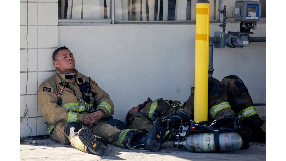 Firefighters rest at outside a cardboard box factory that burned in a wildfire in Riverside, Calif., Oct. 31, 2019. Several blazes broke out in the heavily populated region east of Los Angeles as the Santa Ana winds were predicted to fade.