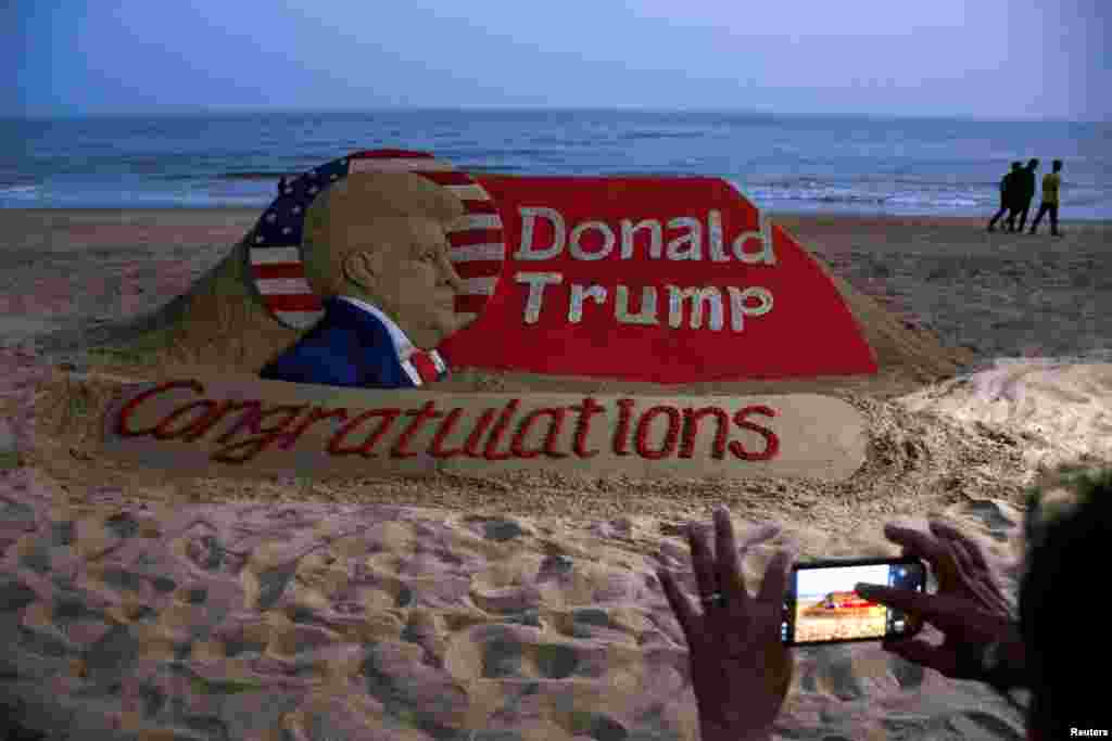 Osoba fotografiše pješčanu skulpturu sa čestitkom Donaldu Trampu, na Puri plaži u Indiji, 6. novembra 2024.