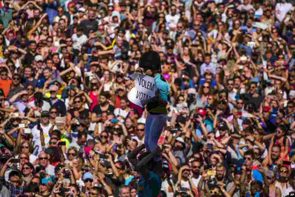 A member of a castelle holds a placard reading in Catalan "We want to vote", as she crowned the human tower in Sant Jaume square in Barcelona, Spain.