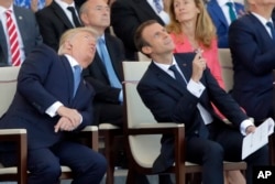 Presiden Donald Trump, saat masa jabatan pertama, dan Presiden Prancis Emmanuel Macron menyaksikan parade militer tradisional Hari Bastille, termasuk jalan layang jet militer, di Champs Elysees di Paris pada 14 Juli 2017. (Foto: Michel Euler/AP Photo)