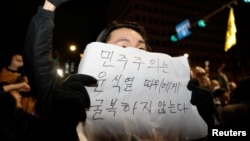 2024年12月4日，南韓總統尹錫烈宣布戒嚴後，大衆聚集在首爾國會大廈，一個人舉著一塊寫著“民主不會向尹錫烈屈服”字樣的標語牌。