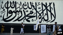 FILE - A vendor selling Taliban flags waits for customers next to a large Taliban flag in Kabul, Afghanistan, on Sept. 24, 2021. 