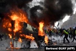 FRANCE -- A man throws a bike in a burning truck during a protest of Yellow vests (Gilets jaunes) against rising oil prices and living costs near the Arc of Triomphe on the Champs Elysees in Paris, on November 24, 2018.