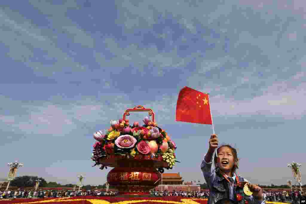 A Chinese girl sits on his father's shoulders near a giant basket decorated with replicas of flowers and fruits on display at Tiananmen Square on China's National Day in Beijing.