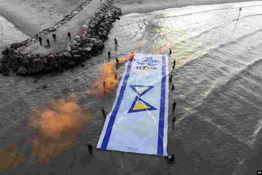 Relatives and supporters of Israelis held hostage by Hamas in Gaza mark 500 days of their captivity by spreading a massive Israeli flag depicting an hourglass in the Mediterranean Sea, in Tel Aviv. Hebrew of the flag reads "Without the abductees, Israel runs out."