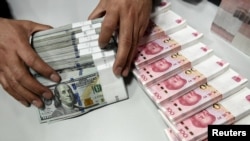 FILE - A clerk counts Chinese yuan and U.S. dollar banknotes at a branch of Bank of China in Taiyuan, China, Jan. 4, 2016. 