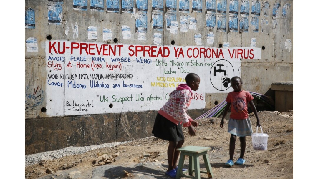 Two young girls sell groundnuts in front of an informational mural advising on precautions to avoid catching the new coronavirus, in the Kibera slum, or informal settlement, of Nairobi, Kenya Thursday, April 2, 2020.