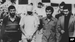 یکی از گروگان‌های سفارت آمریکا در تهران با چشم‌های بسته، به همراه چند تن از انقلابیون طرفدار خمینی - ۹ نوامبر ۱۹۷۹ 