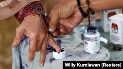 Seorang petugas pemilu membantu seorang perempuan lanjut usia untuk menandai jarinya dengan tinta setelah memberikan suaranya pada Pilkada di Tangerang, Banten, 27 Juni 2018. (Foto: REUTERS/Willy Kurniawan)