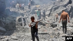 Një djalë mban sende që ka gjetur në rrënojat e një ndërtese të shkatërruar gjatë sulmeve izraelite në kampin e refugjatëve al-Shati në qytetin e Gazës më 22 qershor 2024, ndërsa vazhdon konflikti mes Izraelit dhe grupit militant palestinez Hamas.