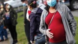 Seorang perempuan hamil mengenakan masker dan sarung tangan memegang perutnya saat mengantre untuk membeli bahan makanan di Gereja St. Mary di Waltham, Massachussetts, 7 Mei 2020. (Foto: AP)
