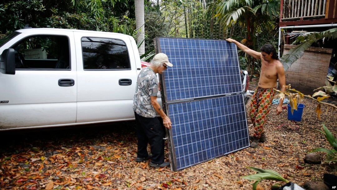Edwin Montoya, left, and Abe Pedro, load a solar panel removed from the Montoya family's property onto a truck, May 18, 2018, near Pahoa, Hawaii. Montoya family owns a farm near Pohoiki Road and lava crossed the road near his property, Friday, blocking access to the neighborhood.