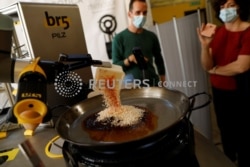 Chef Maria Munoz menyaksikan robot yang dibuat oleh perusahaan Spanyol br5 dan Mimcook membuat paella saat demonstrasi di sebuah gudang di San Fernando de Henares, di luar Madrid, Spanyol, 20 Mei 2021. (Foto: REUTERS/Susana Vera)