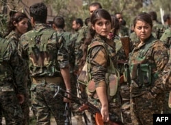 Fighters of the U.S.-backed Kurdish-led Syrian Democratic Forces (SDF), including women, gather to celebrate near the Omar oil field in the eastern Syrian Deir Ezzor province, March 23, 2019, after announcing the total elimination of the Islamic State's self-declared caliphate.