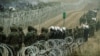 Polish soldiers and police watch migrants at the Poland/Belarus border near Kuznica, Poland, November 11, 2021, in this photograph released by the Territorial Defence Forces. 