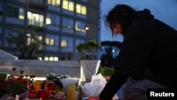 Seorang perempuan meletakkan lilin di patung mendiang Paus Yohanes Paulus II di Rumah Sakit Gemelli, tempat Paus Fransiskus dirawat karena pneumonia, di Roma, 12 Maret 2025. (Foto: Guglielmo Mangiapane/Reuters)